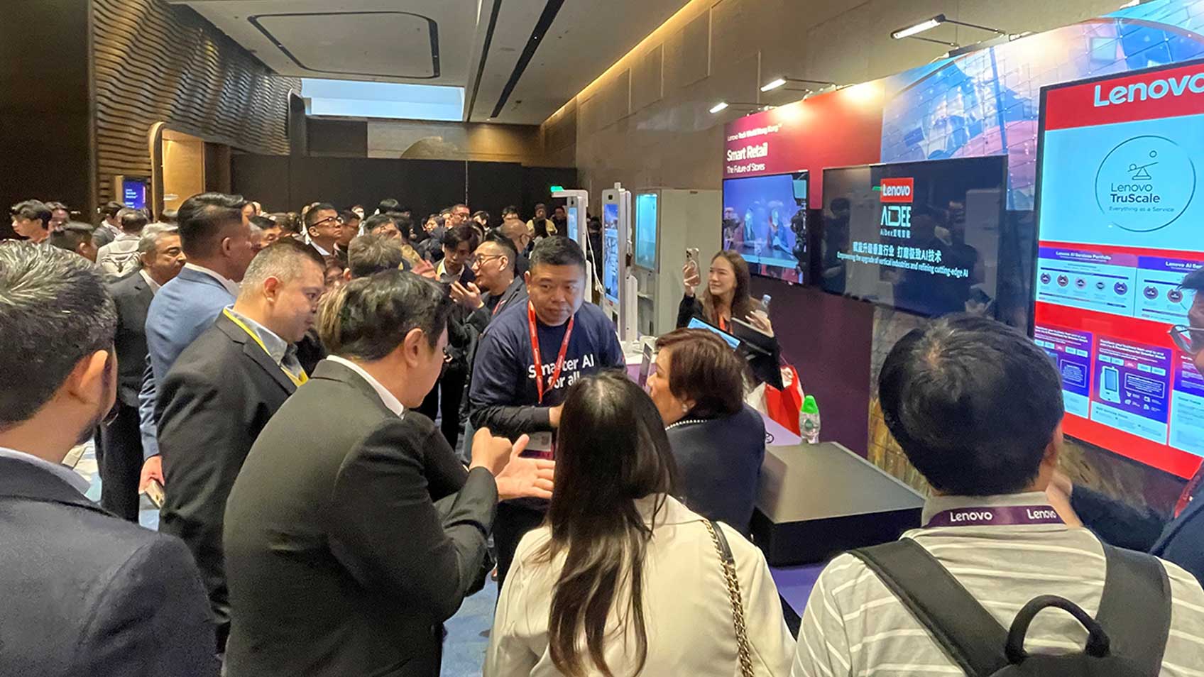 Asistentes al Tech World en Hong Kong agrupados alrededor del stand de Lenovo con varias pantallas. 