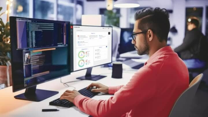 Image of a young professional working in an office in front of dual monitors. 