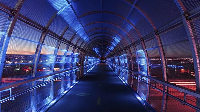 A glass walkway bridge with blue lights over a road at dusk