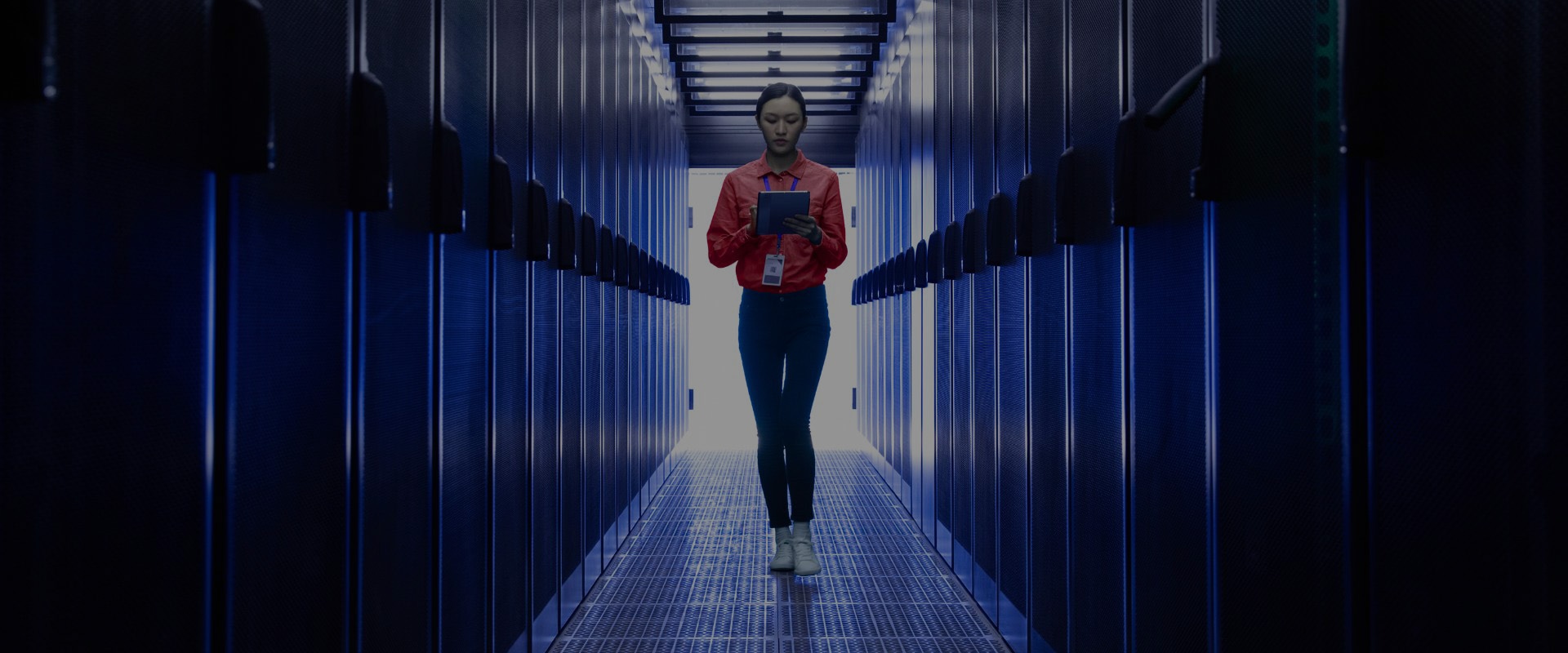 Image of a woman walking in a server room while using a tablet.