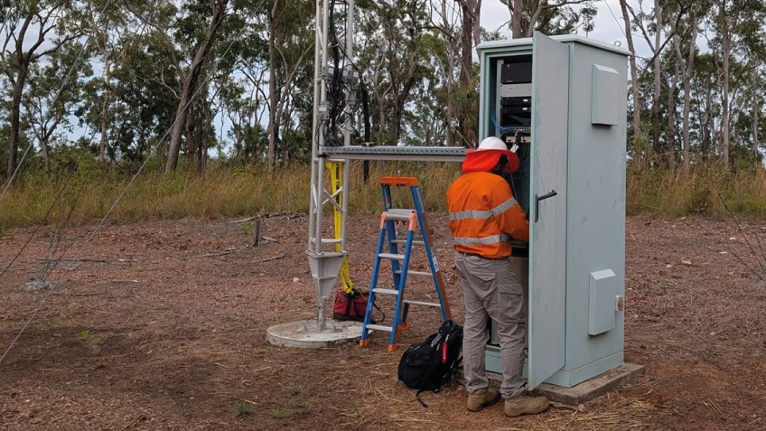 Field technician works on an outdoor equipment cabinet beside a tower.