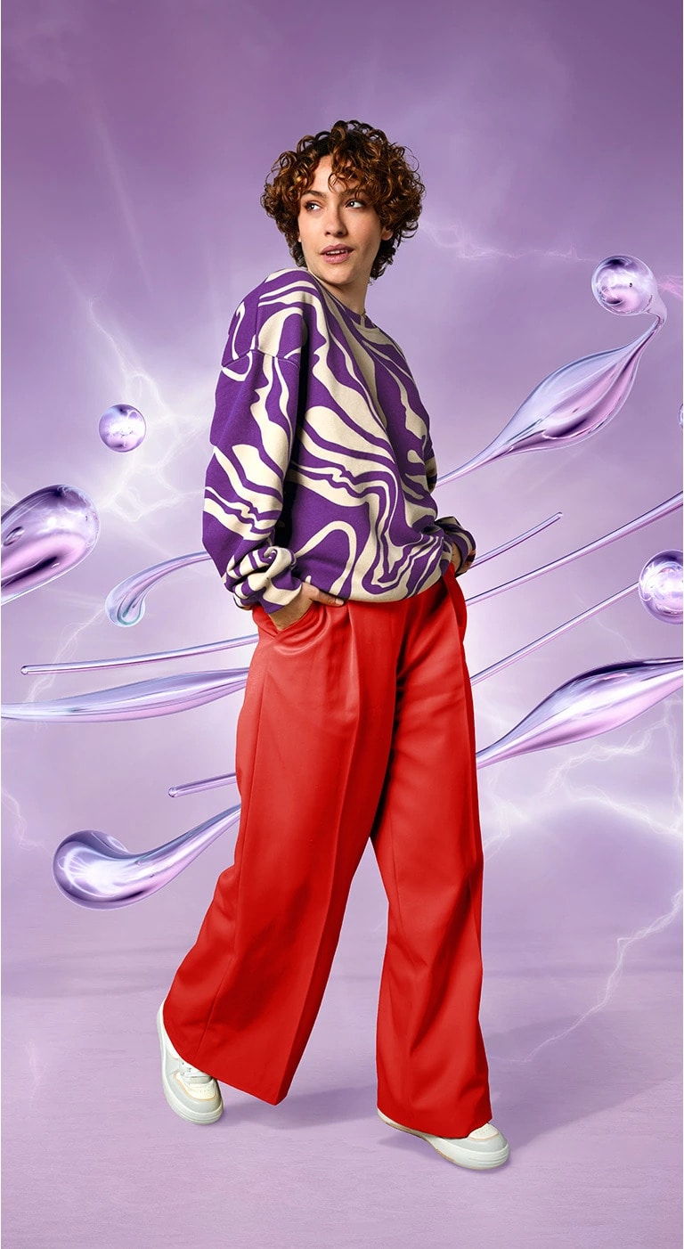 Fashionably dressed person, facing forward and wearing bright colors against a lilac digitally rendered water-drop-swoosh background.