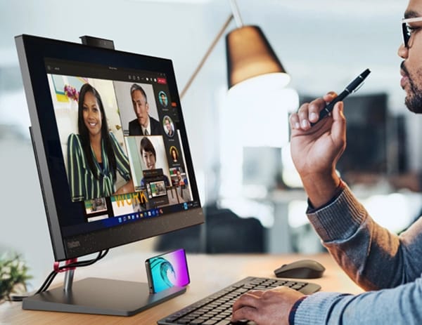 Gerente de oficina en una videoconferencia a través de un PC todo en uno ThinkCentre Neo 50a, con el teléfono (vendido por separado) en el portateléfono y un lápiz (vendido por separado) en la mano.