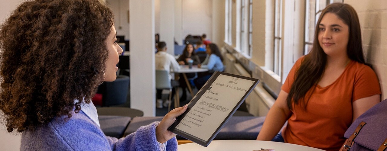 Two people in a café, one holding a Lenovo Smart Paper E-Ink reader & making notes on screen with Lenovo Smart Pen