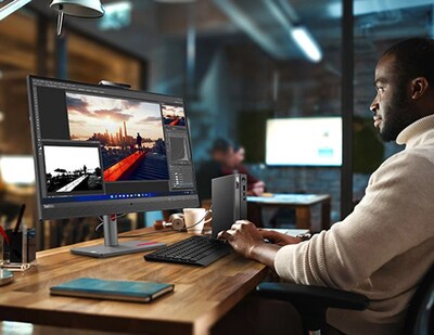 Vista lateral frontal del Lenovo ThinkCentre Neo 50q de 4.ª generación Tiny (Intel), colocado verticalmente sobre un escritorio de oficina, junto a un monitor y un teclado (vendidos por separado), con una persona escribiendo en el teclado