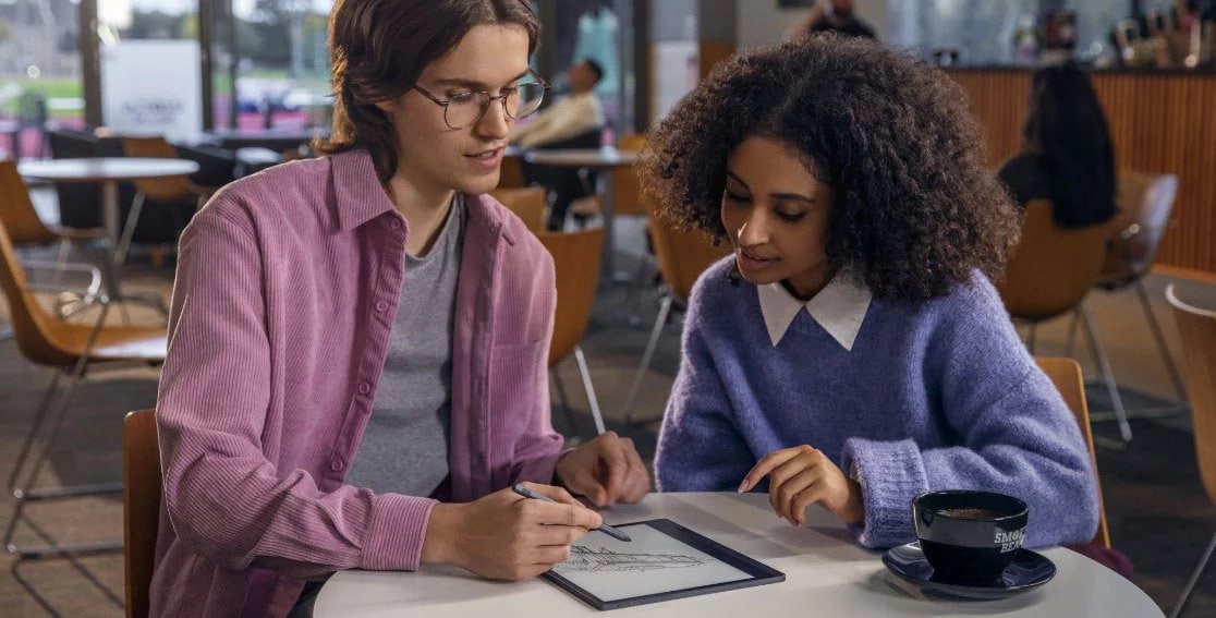 Two students in a cafe with Lenovo Smart Paper E-Ink reader laid flat, with one student making notes on screen with Lenovo Smart Pen