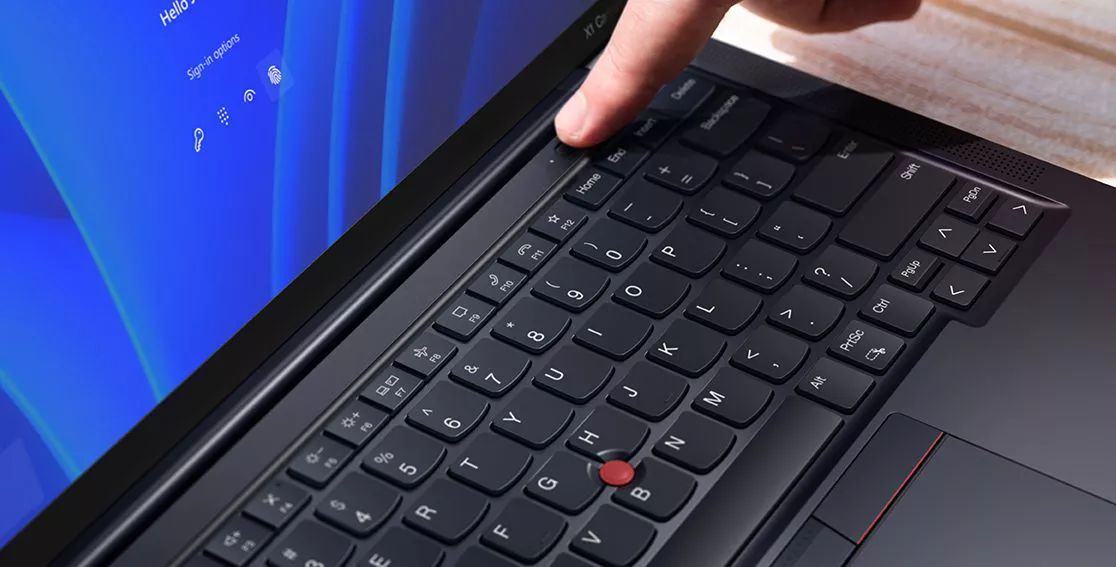 Tightly cropped shot of a Lenovo ThinkPad X1 Carbon laptop keyboard, with a person's hand placing the finger on the power button/fingerprint reader 