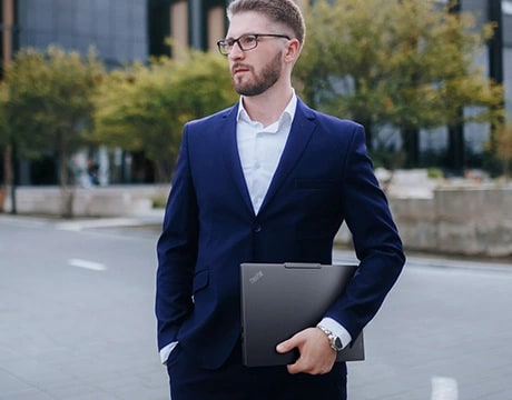 一位男子站在城市街道旁，左手拿著 Lenovo ThinkPad E14 Gen 7 (14 吋 Intel) 筆記型電腦